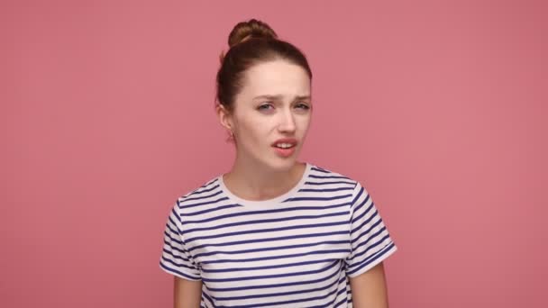 聞こえないわよ 混乱した女性の耳の近くに耳を傾け 耳の問題を聞いて 理解するのは難しいが 縞模様のTシャツを着て手を保つ ピンクの背景に隔離された屋内スタジオショット — ストック動画
