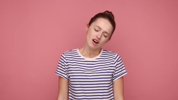 痛みから眉をひそめて 髪パンマッサージ首を持つ不健康な女性は 疲れ労働者の筋肉の緊張 縞模様のTシャツを着て苦しんでいる ピンクの背景に隔離された屋内スタジオショット — ストック動画