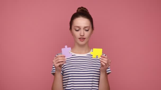髪のパンを保持し 2つのジグソーパズルの作品を示す笑顔の女性 パズルのマッチングと接続 良い結果で問題を解決 ピンクの背景に隔離された屋内スタジオショット — ストック動画