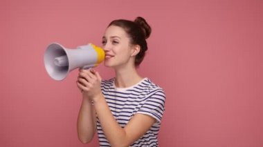 Saçlı çekici bir kadın megafonla konuşuyor, haberleri duyuruyor, yüksek sesle ilan veriyor, hoparlör kullanıyor, çizgili tişört giyiyor. Pembe arka planda kapalı stüdyo çekimleri.