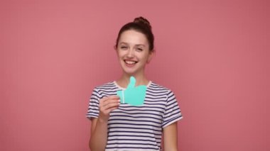 Bun saç stili olan çekici bir kadın kağıt şekilli tabelayı gösteriyor, kamerayı işaret ediyor, çizgili tişört giyiyor. Pembe arka planda kapalı stüdyo çekimleri.