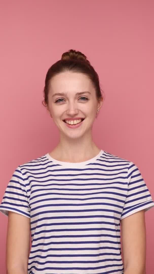 幸せな表情でカメラを見てパンの髪型と笑顔幸せな女性の垂直ショット 縞模様のTシャツを着て ピンクの背景に隔離された垂直スタジオショット — ストック動画