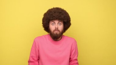 Afro saç stili omuz silken, kafası karışmış ve bilgiden emin olmayan, pembe kazak giyen kafası karışık sakallı bir adam. Sarı arka planda kapalı stüdyo çekimleri.