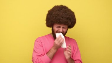 Afro saçlı sakallı, kaşlarını çatmış, gözyaşlarını mendille silen umutsuz, duygusal stresli, kazak giyen bir adam. Sarı arka planda kapalı stüdyo çekimleri.