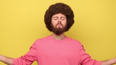 Sakallı adam aklını başına topluyor, ellerini namaste jesti yapıyor, meditasyon yapıyor, yoga nefes alma tekniği stresi azaltıyor, pembe kazak giyiyor. Sarı arka planda kapalı stüdyo çekimleri.