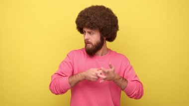 Afro saçlı sakallı bir adam yoga pozunda duruyor ve gergin bir günden sonra rahatlamaya ve sakinleşmeye çalışıyor, pembe kazak giyiyor. Sarı arka planda kapalı stüdyo çekimleri.