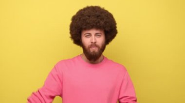 Sakallı, Afro saçlı, el hareketleriyle resim çerçeveli parmaklarından bakıp pembe kazak giyen ilginç bir ana odaklanan bir adam. Sarı arka planda kapalı stüdyo çekimleri.