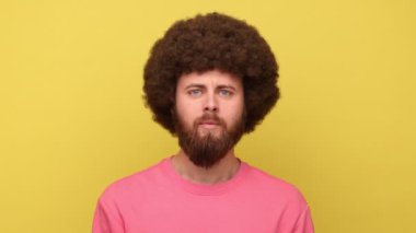 Sakallı, sakallı, Afro saçlı, kameraya bakıp bağıran sinirli, kötü ruh halinde pembe kazak giyen bir adam. Sarı arka planda kapalı stüdyo çekimleri.