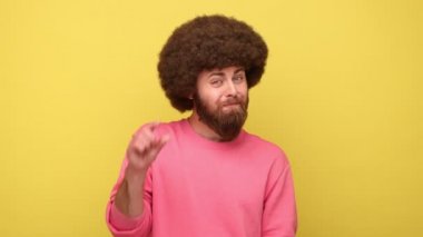 Afro saç stili sakallı, hayal kırıklığına uğramış bir adam. Biraz jest yapıyor. Düşük reytingli, ölçülü, pembe kazak giyen bir adamdan memnun değil. Sarı arka planda kapalı stüdyo çekimleri.