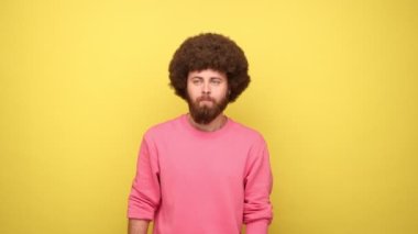 Afro saçlı, yüzü pozitifli, ellerini kaldıran dubdance hareketi yapan, dans pozu veren, pembe kazak giyen bir adam. Sarı arka planda kapalı stüdyo çekimleri.