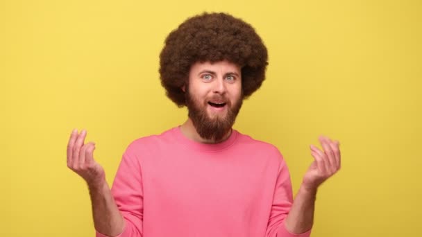 アフリカのヘアスタイルを持つ髭の男は お金のジェスチャーを示す指をこすり 給与を待って 想像上の紙幣を投げ ピンクのスウェットシャツを着ている 黄色の背景に隔離された屋内スタジオショット — ストック動画