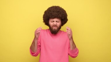Afro saç stili masaj yapan, baş ağrısı çeken, migreni olan, yüksek tansiyonu olan, konsantre olmaya çalışan, pembe kazak giyen bir adam. Sarı arka planda kapalı stüdyo çekimleri.