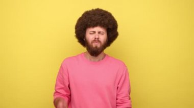 Afro saç stili, yanak ağrısı çeken, akut diş ağrısı çeken, periodontal hastalık geçiren, diş çürüğü ya da çene ağrısı olan pembe kazak giyen hippi bir adam. Sarı arka planda kapalı stüdyo çekimleri.
