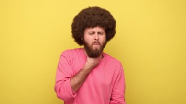 Boğaz ağrısı. Afro saçlı, boynu sakat, boğazında korkunç bir ağrı, sağlık sigortası ve medikal konsepti olan pembe kazak giyen hippi bir adam. Sarı arka planda kapalı stüdyo çekimleri