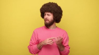 Sakallı hippi dalgın, Afro saç stili parmaklarını büken, tefekkür eden, hesaplayan, pembe kazak giyen bir hippi. Sarı arka planda kapalı stüdyo çekimleri.