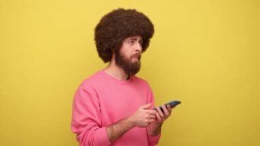 Afro saç stili bir hippi cep telefonuyla mesaj yazıyor, bilgi üzerine sohbet ediyor, seçim yapıyor, kuşkuları var, pembe kazak giyiyor. Sarı arka planda kapalı stüdyo çekimleri.
