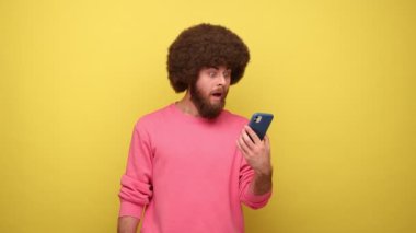 Afro saçlı hippi bir adam alışveriş torbalarını ve boş ekranlı akıllı telefonları gösteriyor. İnternetten alışveriş yapıyor, reklam yapıyor, kazak giyiyor. Sarı arka planda kapalı stüdyo çekimleri.