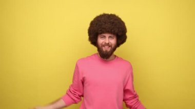 Afro saçlı sakallı hippi Amerikan bayrağı taşıyor ve kameraya mutlu bir şekilde bakıyor, ulusal bayramı kutluyor, pembe kazak giyiyor. Sarı arka planda kapalı stüdyo çekimleri.