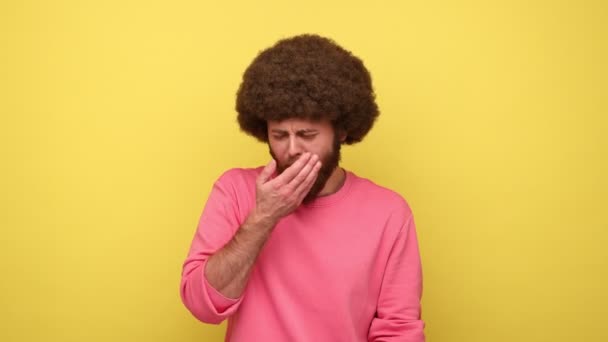 寒さから震えてアフロヘアスタイルを持つ髭の男は ピンクのスウェットシャツを着て 季節のインフルエンザの症状に苦しんでいない感じ 黄色の背景に隔離された屋内スタジオショット — ストック動画