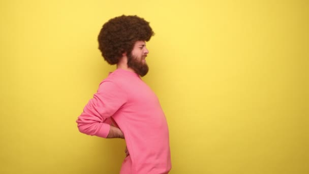 腎臓の損傷 腰痛に手を取り ピンクのトレーナーを身に着けているアフロヘアスタイルを持つ髭のヒップスター男性のサイドビュー 黄色の背景に隔離された屋内スタジオショット — ストック動画