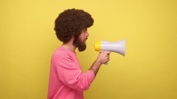 メガホンで話すアフロの髪型と穏やかなハンサムな男の側のビューは ピンクのスウェットシャツを着て 重要な情報を発表した 黄色の背景に隔離された屋内スタジオショット — ストック動画