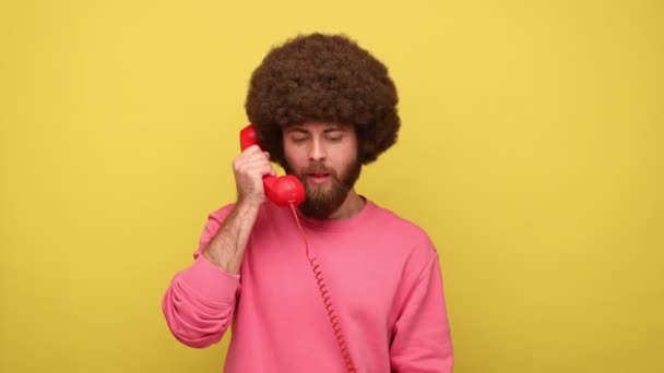 留着胡子的嬉皮士男人 有着非洲式的尖叫和大喊 讲着复古的固定电话 抱怨连接质量 穿着粉色运动衫 在黄色背景下隔离的室内拍摄 — 图库视频影像