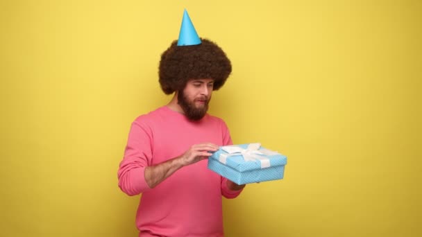 Bärtiger Hipster Mann Mit Party Kegel Öffnet Geburtstagsgeschenkbox Und Lugt — Stockvideo