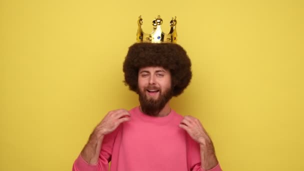 アフリカの髪型と彼の頭の上に黄金の冠を持つ利己的な男は ピンクのスウェットシャツを着て 自分自身を指して 彼の権威 Vサインを示しています 黄色の背景に隔離された屋内スタジオショット — ストック動画