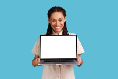 Siyah rastalı mutlu kadın yeni bir cihazın reklamını yapıyor, elinde boş ekranlı dizüstü bilgisayar var, tatmin olduğunu ifade ediyor, beyaz gömlek giyiyor. Mavi arka planda kapalı stüdyo çekimi.