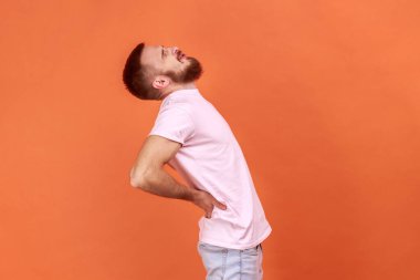 Sağlıksız bir adamın sırtına dokunması, bel ağrısının azalması, kas ağrısı, omurga diski yaralanması, pembe tişört giymesi. Turuncu arka planda kapalı stüdyo çekimleri.