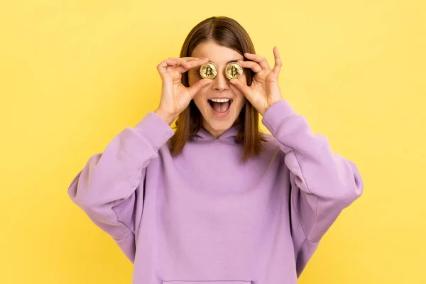 ゴールドビットコイン ブロックチェーンコンセプト 暗号通貨 デジタルマネーで目をカバーする幸せな笑顔の女性の肖像画 紫色のパーカーを着て 黄色の背景に隔離された屋内スタジオショット — ストック写真