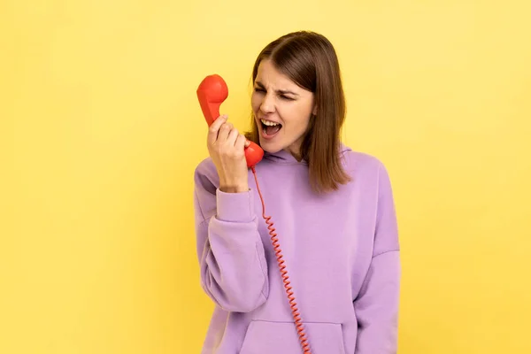 住宅整備コールセンター 怒って茶色の髪の女性がレトロな携帯電話に叫んで 顧客の呼び出しに苛立ち 紫色のパーカーを着て 黄色の背景に隔離された屋内スタジオショット — ストック写真