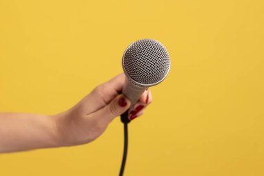 Mikrofon tutan kadının yakın plan portresi, NP sorusunu cevaplıyor. Sarı arka planda kapalı stüdyo çekimleri.