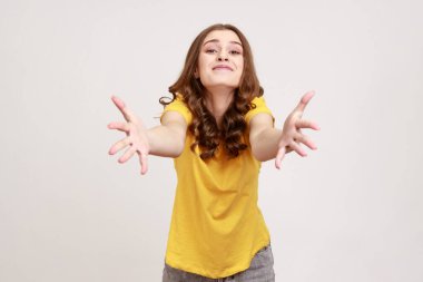 Lütfen, bedavaya alın! Nazik, cömert, dalgalı saçları olan, kucaklamayı öneren, misafirperver bir yüz ifadesiyle davet eden bir kadın. Gri arka planda izole edilmiş kapalı stüdyo görüntüleri.
