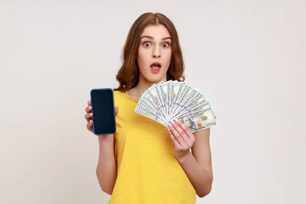 수익성 서비스 달러와 스마트폰을 티셔츠를 소녀가 모바일 애플리케이션으로 은회색 배경에 — 스톡 사진