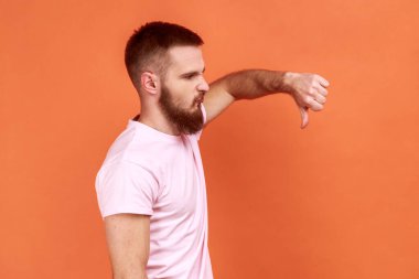 Kötü kaliteyi eleştiren, hoşnutsuz suratını buruşturan, hoşnutsuzluk gösteren, onaylamadığını ifade eden, pembe tişört giyen bir adamın yan görünüşü. Turuncu arka planda kapalı stüdyo çekimleri.