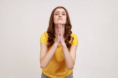 Lütfen, affınıza sığınıyorum! Sevimli üzgün, genç, üzgün, dalgalı saçlı, çaresiz suratını ekşiten ve yardım için dua eden bir kadın. Gri arka planda izole edilmiş kapalı stüdyo görüntüleri.