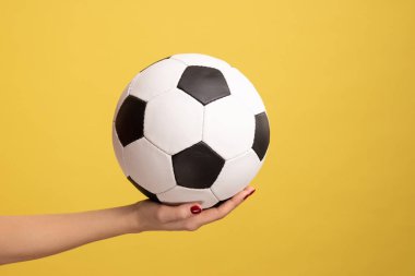 Profile side view closeup of woman hand holding football or soccer ball, supporting favorite football team on match. Indoor studio shot isolated on yellow background.