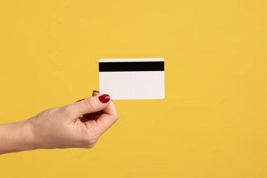 Profil yan görüntüsü, insan elinin klasik kredi kartını tutarken, para kazanırken, bankacılık yaparken. Sarı arka planda kapalı stüdyo çekimleri.