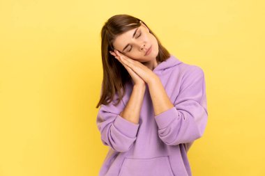Yorgun, genç bir kadının portresi uyuyor, avuçlarına uzanıyor, gözlerini kapalı tutuyor, mor kapüşonlu giyiyor. Sarı arka planda kapalı stüdyo çekimleri.