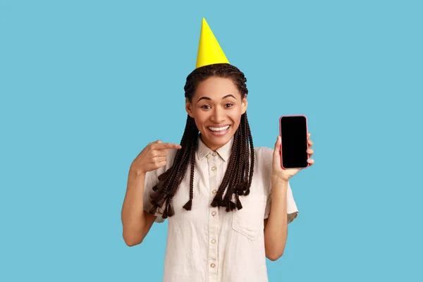 Усміхнена Щаслива Жінка Чорними Дредлоками Жовтим Партійним Конусом Показує Телефон — стокове фото