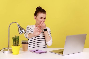 Displeased woman office worker holding breath, pinching her nose with fingers, confused with disgusted odor, dont want to breath. Indoor studio studio shot isolated on yellow background.