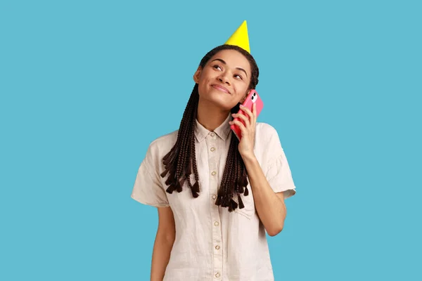 头戴派对圆锥帽的女人的画像 面带微笑抬起头 欢度节日 打电话祝贺 穿白衬衫 室内拍摄被蓝色背景隔离 — 图库照片