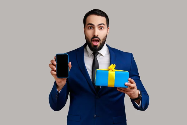 Shocked Businessman Holding Gift Box Cell Phone Empty Display Online — Stok fotoğraf