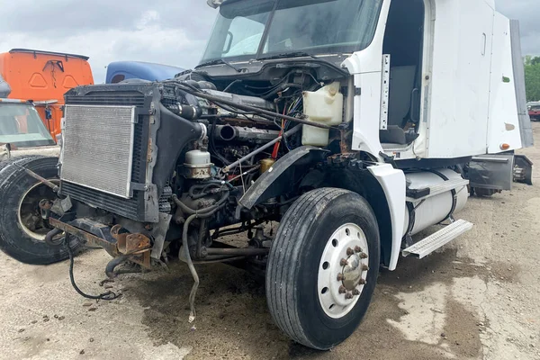 Big external damage of truck, wrecked bumper and car fender missing, broken automobile after road crash, outdoor park with automobile wreckage parts debris