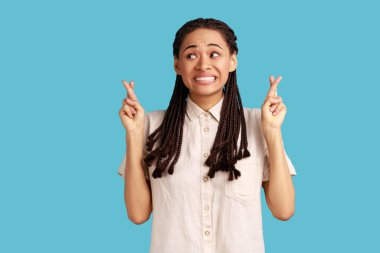 Siyah saçlı genç bir kadın iyi şansa inanmayı diliyor, hayallerin gerçekleşmesini umuyor, umut dolu bir ifadeye sahip, bir şeyler bekliyor. Mavi arka planda kapalı stüdyo çekimi.