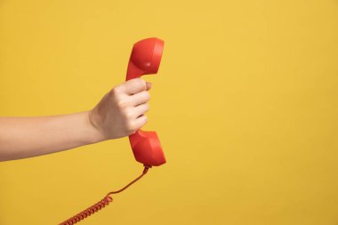 Profil yan görüntüsü, kadının el ele tutuşmasını ve kırmızı telefon ahizesini gösteriyor. Sarı arka planda kapalı stüdyo çekimleri.