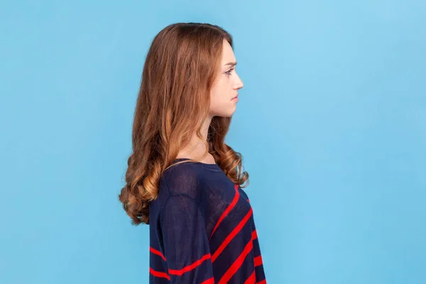 悲しい動揺若い女性が前を見て立って縞模様のカジュアルなスタイルのセーターを着てのサイドビューは 気分が悪く うつ病に苦しんでいる 青い背景に隔離された屋内スタジオショット — ストック写真