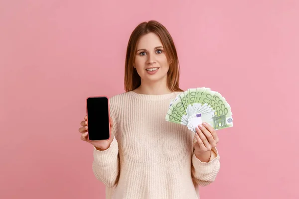 지폐와 화면으로 온라인 뱅킹을 스웨터를 휴대폰을 여성의 스튜디오 배경에서 고립되어 — 스톡 사진