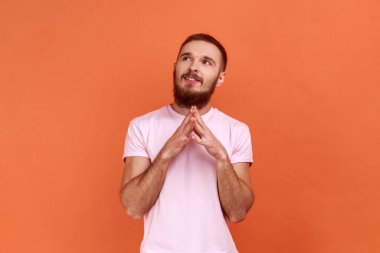 Sakallı adamın portresi gelecek için plan yapan düşünceli adam iyi bir iş hayali kuran, başka tarafa bakan, pembe tişört giyen. Turuncu arka planda kapalı stüdyo çekimleri.